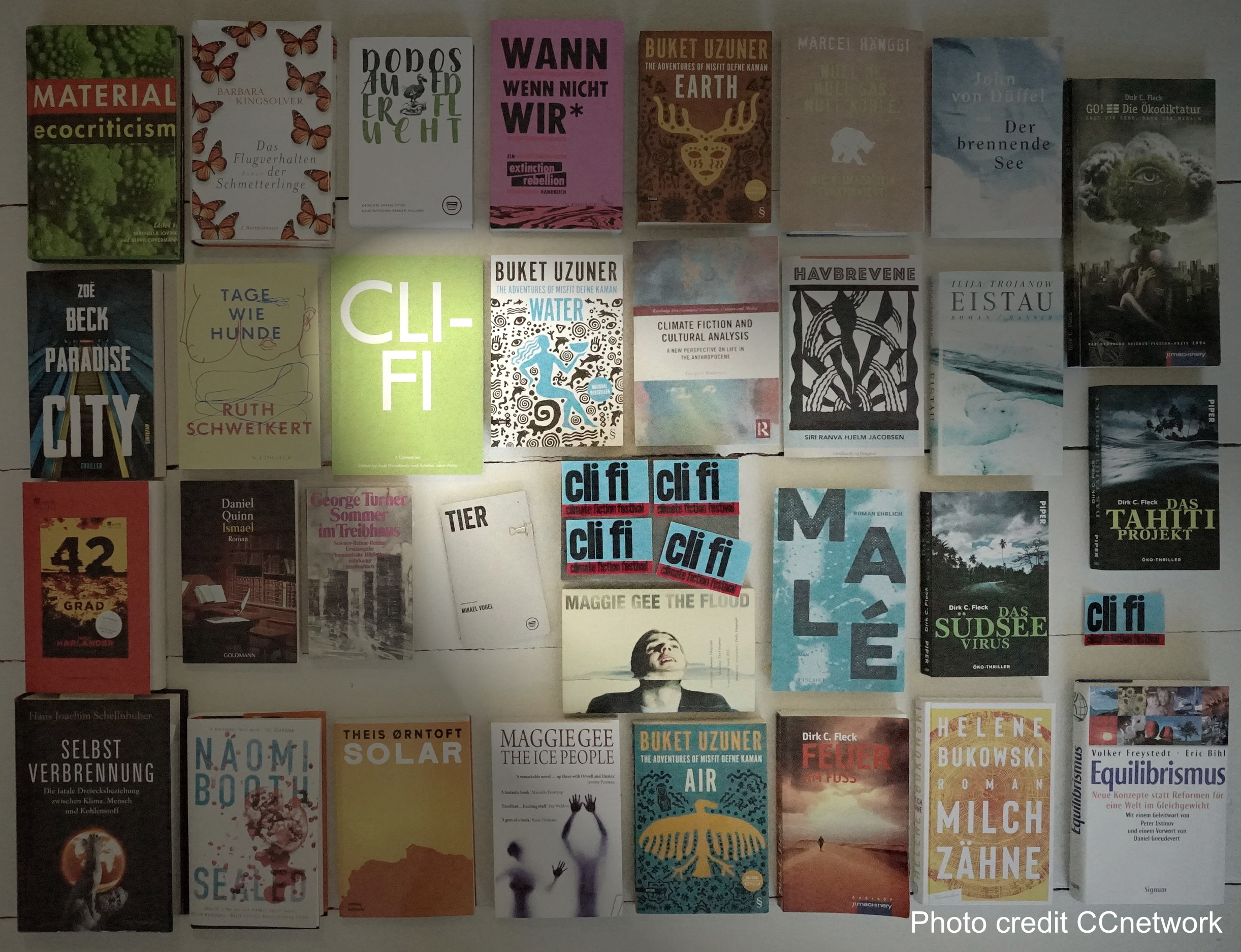 30 Bücher aus dem großen Feld der Klimaliteratur liegen nebeneinander auf dem Boden. In der Mitte beleuchtet ein Spottlicht
ein Cover mit der Abkürzung cli fi