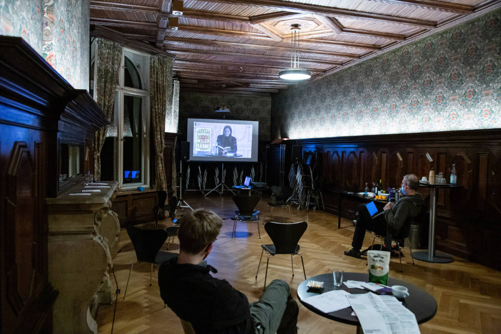 Das leere Kaminzimmer im Literaturhaus Berlin. Zwei Personen schauen sich den Live-Stream an